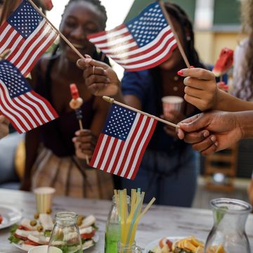 candid shot of diverse group of joyful young people, friends, having fun, dancing and waving american flags while celebrating 4th of july on the balcony