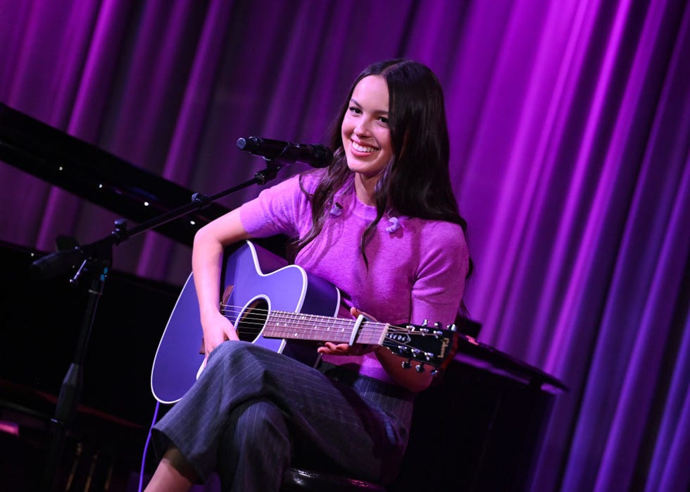 olivia rodrigo performs onstage at the drop olivia rodrigo at the grammy museum in a purple tee with a purple guitar