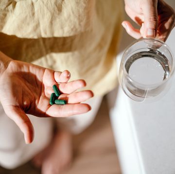 a woman standing at a table with green pills in her hand taking vitamins, macro elements, chlorophyll, spirulina and bioactive supplements to maintain health prevention of colds during an epidemic the first symptoms of incipient menopause are hypotension or hypertension, hot flashes