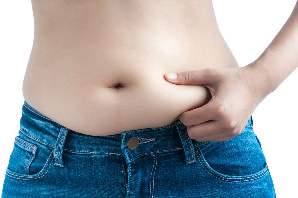 a woman wearing blue jeans pinches her belly fat