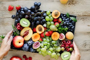 close up of a woman hands holding fruit tray on wooden table female with different types of fruits in a tray