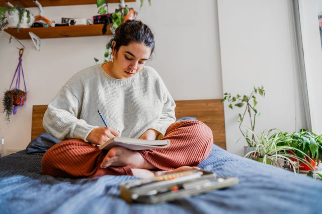 young woman sitting on the bed drawing in notepad in the bedroom