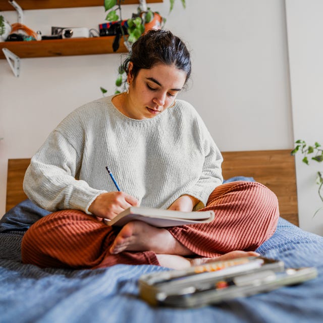 Young woman sitting on the bed drawing in notepad in the bedroom young woman sitting on the bed drawing in notepad in the bedroom