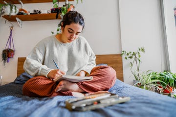 young woman sitting on the bed drawing in notepad in the bedroom