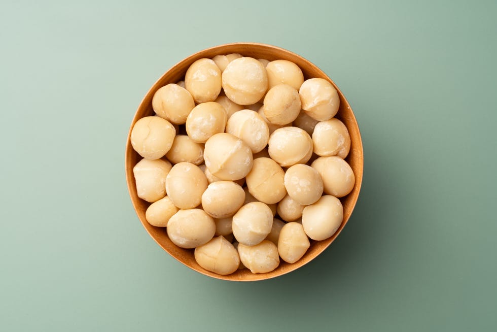 macadamia nuts in wooden bowl on green background directly above view