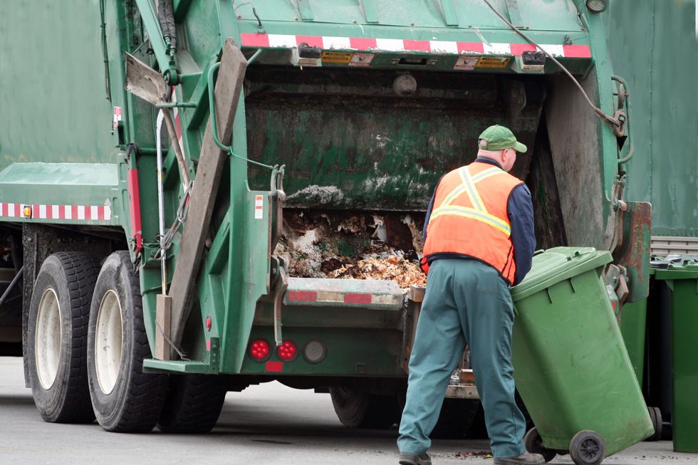 waste management worker positions green bin on the automatic dumper at the back of truck