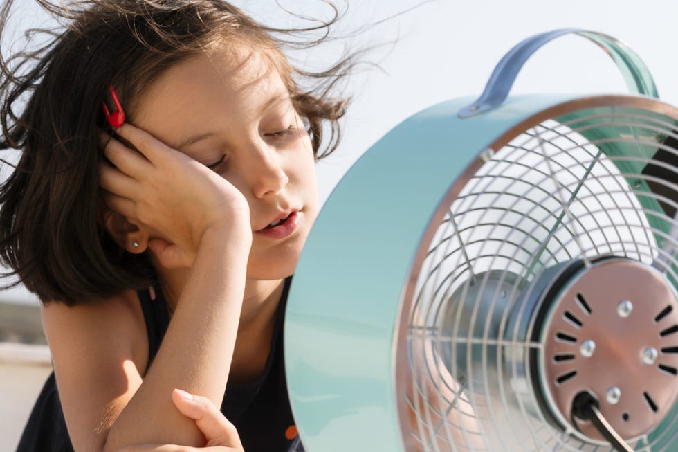 overheated little child is sitting in front of electric fan trying to cool down.