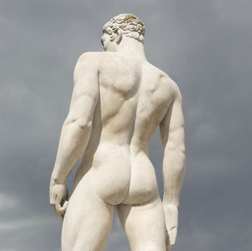 statue of a muscular male athlete warms his buns against moody gray sky