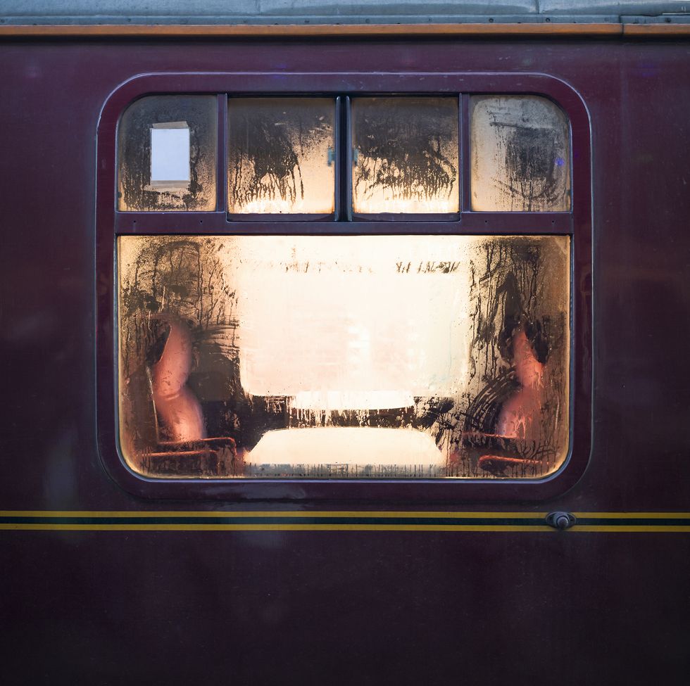 looking through the glowing window of an old fashioned train carriage at tables and seats, with water condensation on the window