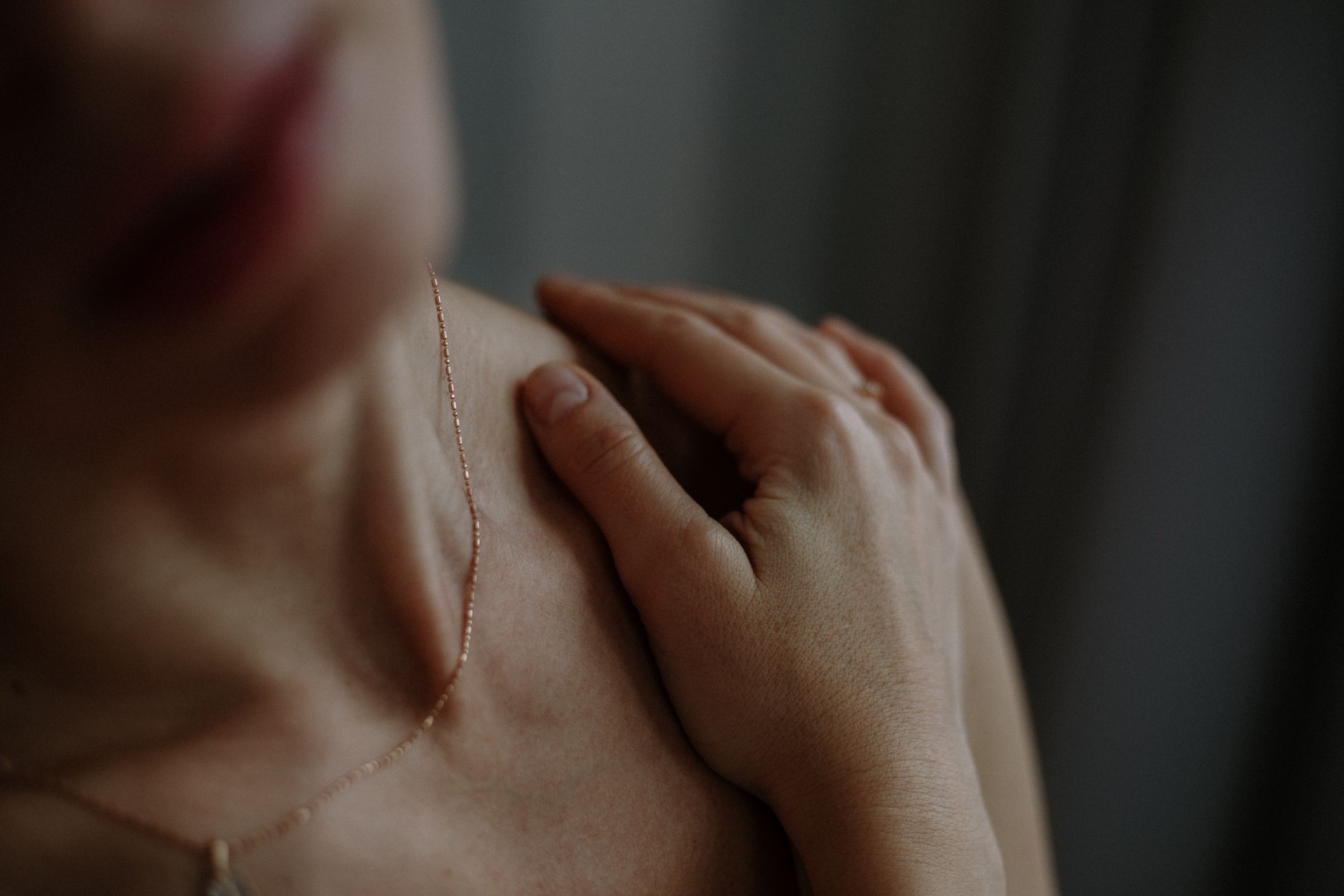 close up photo of unrecognizable naked woman with hand delicately resting on shoulder, evoking sense of contemplation dimmed natural light accentuates calmness of scene, inviting viewers into moment of self reflection and repose