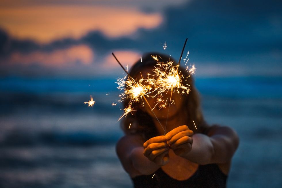 happy young woman holding sparkler celebrating new years eve on the beach