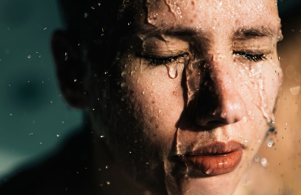 a beautiful and serene european woman is taking a shower, water flowing over her face, her eyes closed daily hygiene and relaxing self care routine to take stress and problems away close up with space for text copy