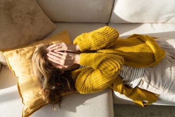 tired woman lying on sofa while holding hands on her face
