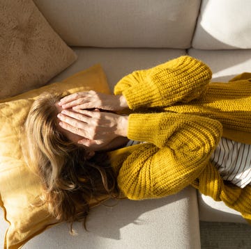 Sick oman lying on sofa and covering her eyes with hands tired woman lying on sofa while holding hands on her face