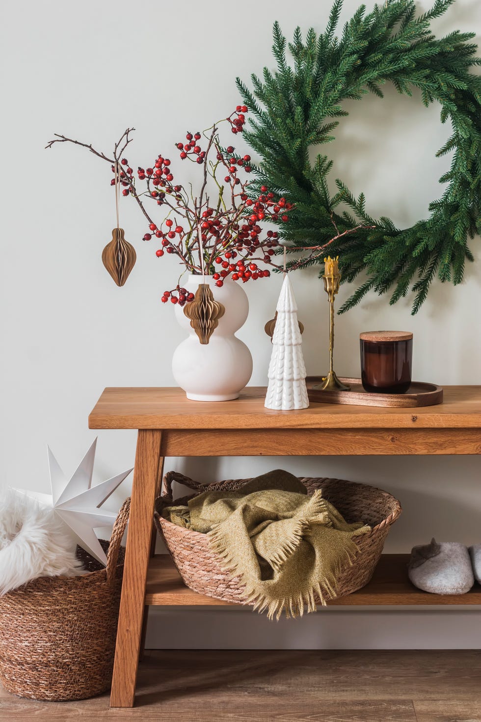 Christmas interior - oak bench with Christmas decor, candles, basket with blankets, Christmas tree wreath on the wall christmas interior oak bench with christmas decor, candles, basket with blankets, christmas tree wreath on the wall