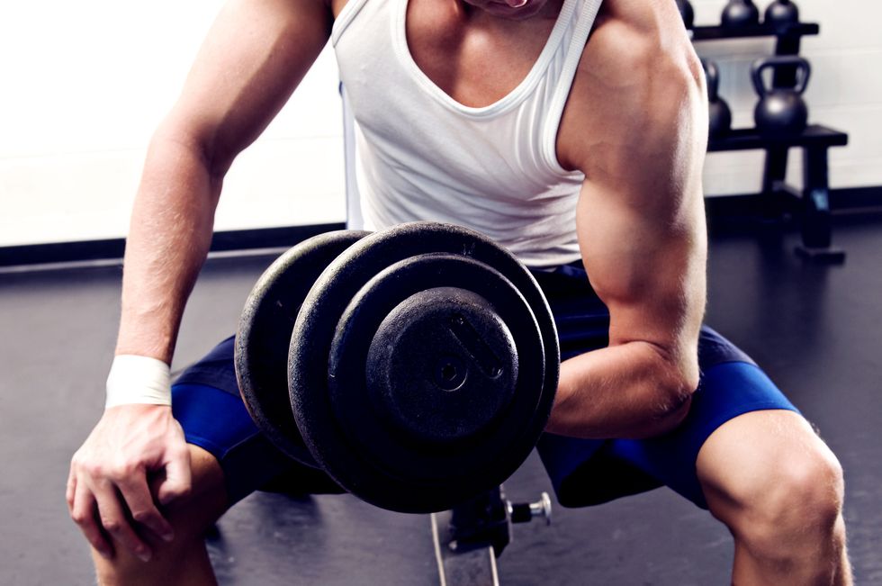 man performing a bicep curl with a dumbbell in a gym kettle bells in the background close up