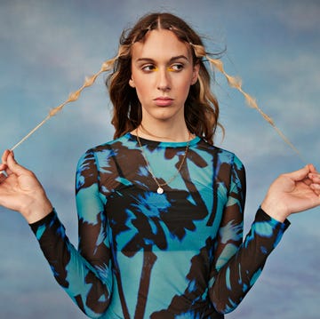 female transgender holding hair against colored background