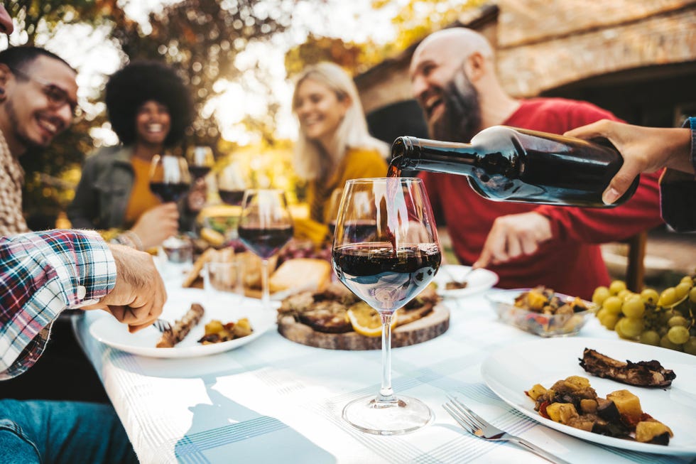 happy friends having bbq dinner party in garden restaurant cheerful family drinking red wine together sitting at dining table food and beverage concept with guys and girls eating fresh meal