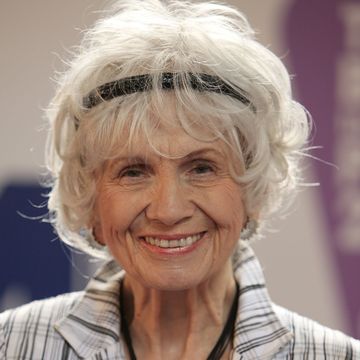 alice munro smiles at the camera, she wears a black headband and a striped suit jacket