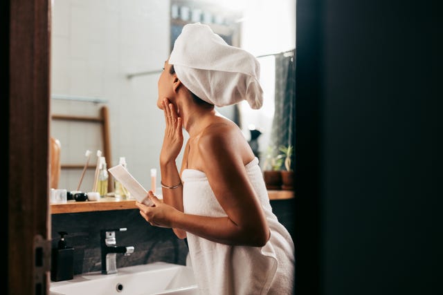 a side view of an attractive asian female taking care of her skin while standing in the bathroom after having a shower skincare concept