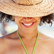 woman of color wearing sun hat over eyes while smiling