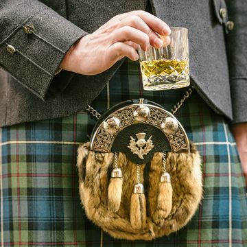 close up of a man wearing a kilt and sporran, holding a dram of scotch whisky
