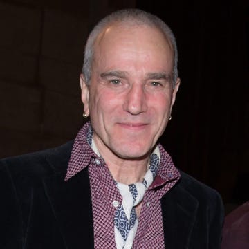 daniel day lewis smiles at the camera, he wears a black blazer, patterned purple collared shirt and blue and white bandana around his neck