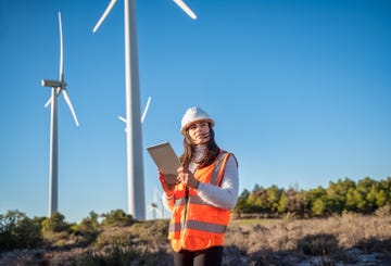 windmill on farm, white woman in clean energy typing on digital tablet and electricity generation with wind turbines in spain renewable power, female engineer in agriculture environment and safety gear  copy space in clear blue sky