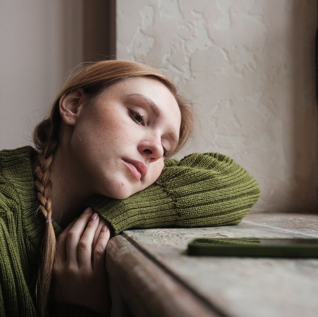 upset redhead woman sitting by window looking at mobile phone waiting call from boyfriend, feeling sad and depressed looking at smartphone waiting for sms message social media depression