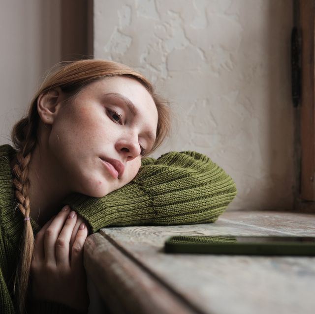 upset redhead woman sitting by window looking at mobile phone waiting call from boyfriend, feeling sad and depressed looking at smartphone waiting for sms message social media depression