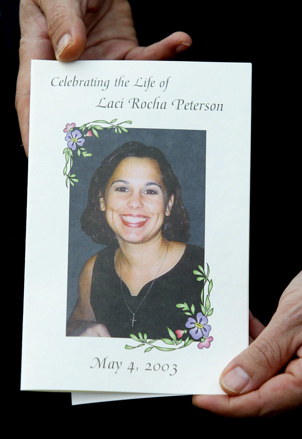 a person holds a paper program in their hands with a photo of laci peterson smiling