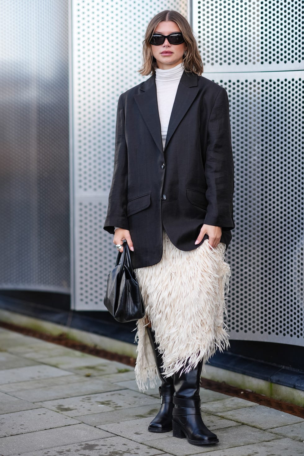 copenhagen, denmark february 01 a guest wears sunglasses, silver earrings, a piercing, a white turtleneck, a black oversized blazer jacket, a white fluffy fringed skirt , a black leather bag, knee high leather boots outside munthe, during the copenhagen fashion week aw24 on february 01, 2024 in copenhagen, denmark photo by edward berthelotgetty images