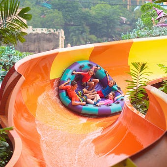 LOW RES UNTIL APPROVAL kids on water slide in outdoor swimming pool. family in aqua theme park. children have fun in splash playground. summer vacation with child. kid on inflatable tube sliding into a pool.