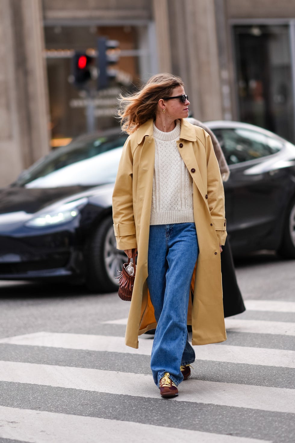 copenhagen, denmark january 31 a guest wears sunglasses, a white knit wool pullover , a yellow trench long coat , blue flared denim jeans pants, brown sneakers shoes, brown leather bag with fringes, outside the garment, during the copenhagen fashion week aw24 on january 31, 2024 in copenhagen, denmark photo by edward berthelotgetty images