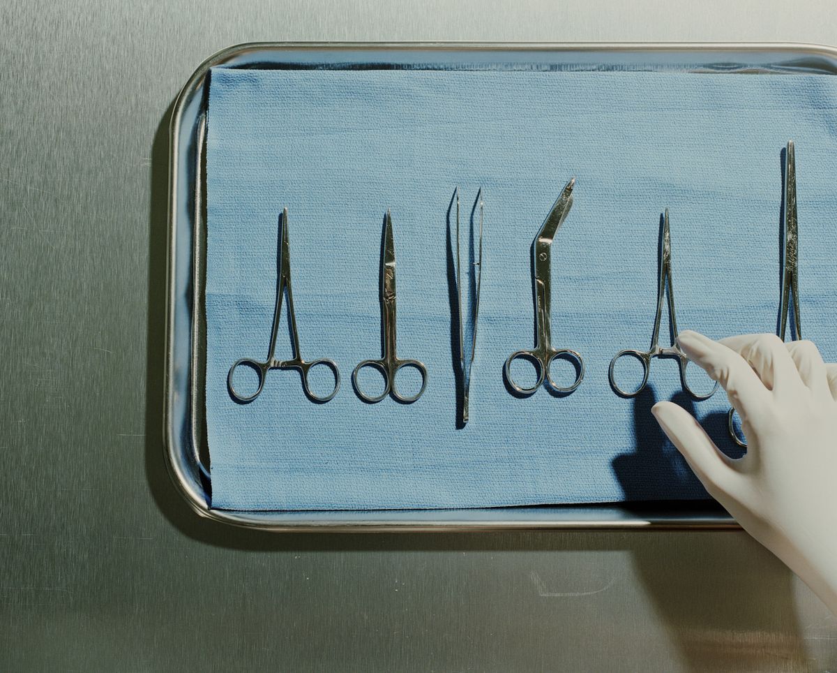 gloved hand reaches for medical scissors on a metal tray