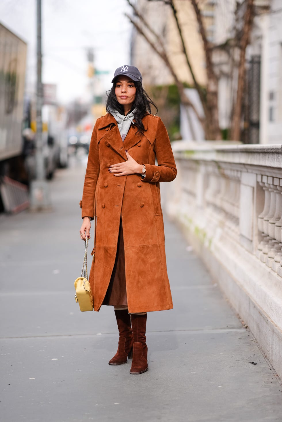 new york, new york february 12 a guest wears a ny cap hat, a gray hoodie sweater , a brown  orange suede trench long coat , a yellow leather bag, brown dark suede boots , outside coach, during new york fashion week, on february 12, 2024 in new york city photo by edward berthelotgetty images