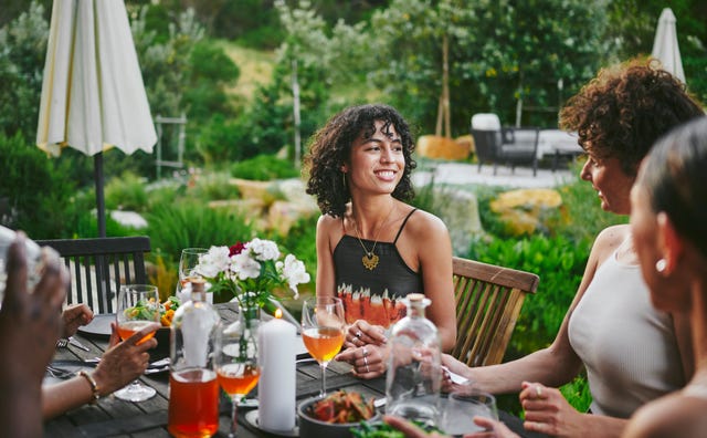 smiling young woman talking with a group of female friends during a dinner party outside on a patio in the early evening