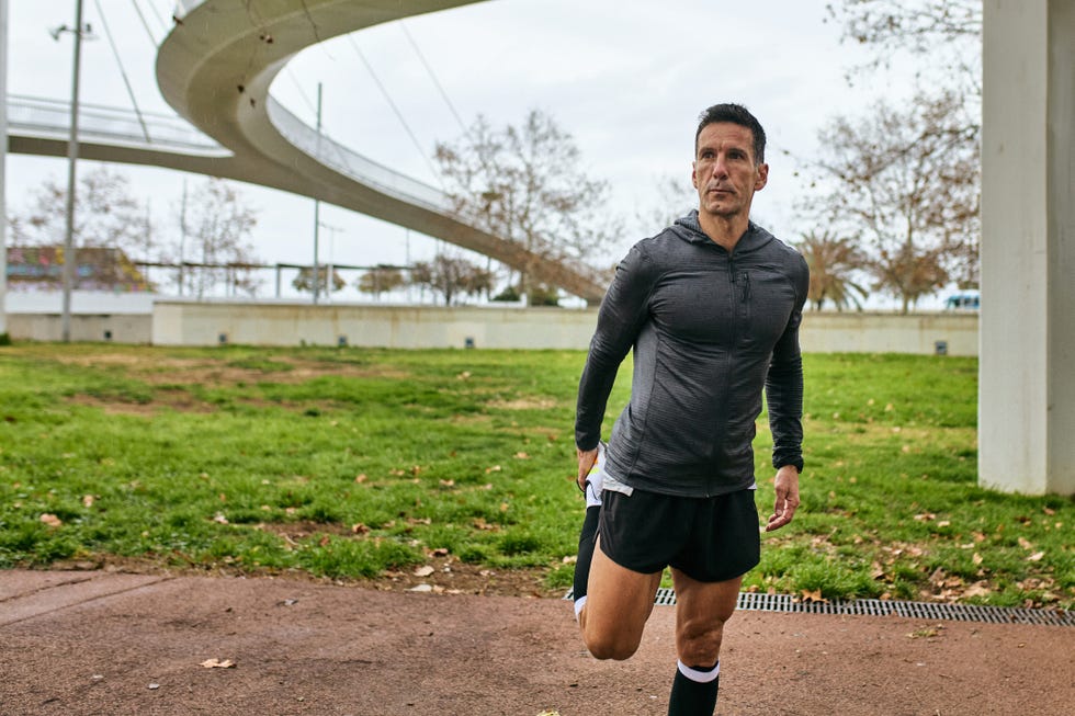 front view of mature man in sports clothing standing outdoors, preparing for afternoon workout, looking away, footbridge in background