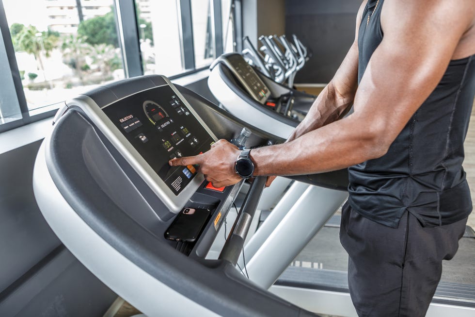 a man dressed in sports clothes starts a treadmill inside a gymnasium the treadmill display shows his speed and distance covered