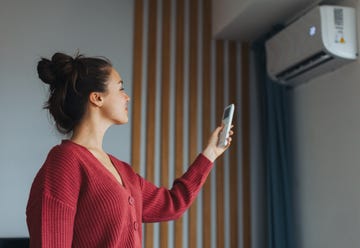heat pump in air conditioning system. woman adjusting temperature, holding remote controller. using heat pump for heating, cooling in modern house. environmentally friendly and sustainable solution for smart home.