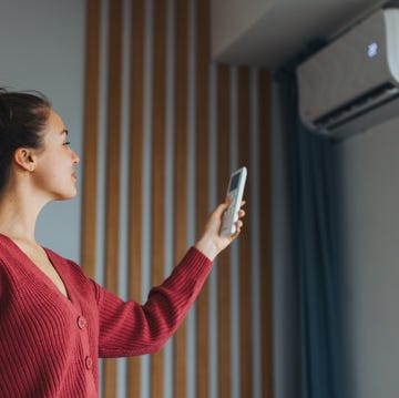 Pros and cons for installing at-home air con heat pump in air conditioning system. woman adjusting temperature, holding remote controller. using heat pump for heating, cooling in modern house. environmentally friendly and sustainable solution for smart home.