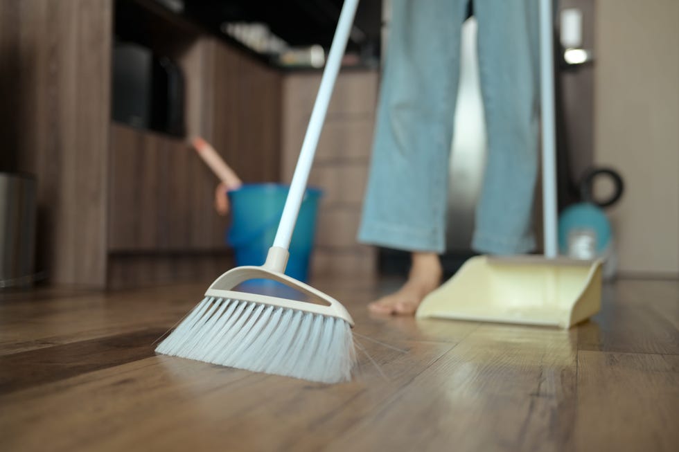 young woman doing chores in kitchen sweeping floor with broom.