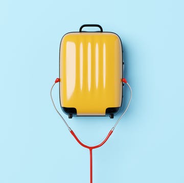 Travel health insurance conceptual image of a yellow suitcase with a stethoscopes earpiece around it with a blue background to illustrate ideas around travel and health insurance