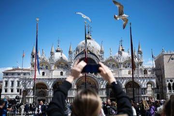 a woman uses her smartphone to take footage of the basilica with flying gulls in san marco square in venice, on april 25, 2024 the new strategy to lower the number of tourists visiting the unesco world heritage site calls for day trippers to pay a five euro ticket to enter the historic city centre and is due to start on april 25 photo by marco bertorello afp photo by marco bertorelloafp via getty images