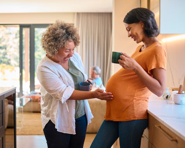 multi generation family at home with grandmother touching pregnant mother's tummy