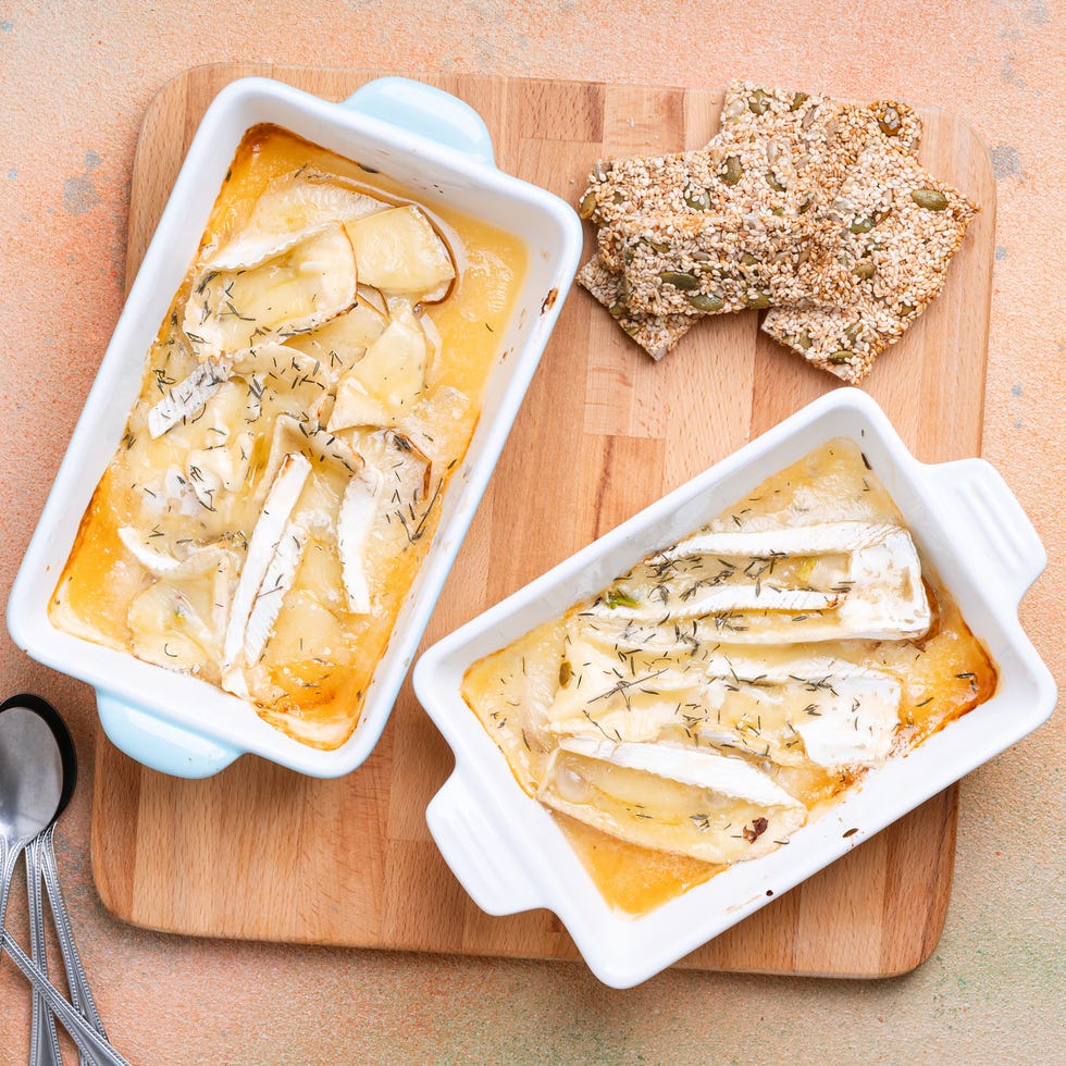 baked brie with pears, honey, and herbs in baking dish, served with homemade healthy seed crackers on wooden board viewed from above