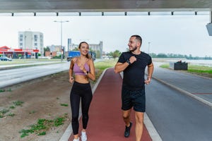 a young man and woman are jogging together on a red track with urban buildings in the background they seem to be enjoying their fitness routine