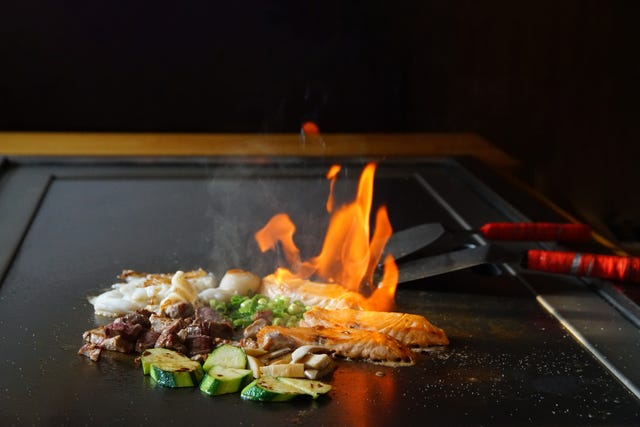 chefs hands with spatula over teppanyaki cooking vegetables meat and seafood on hot hibachi grill table traditional japanese cuisine teppan show