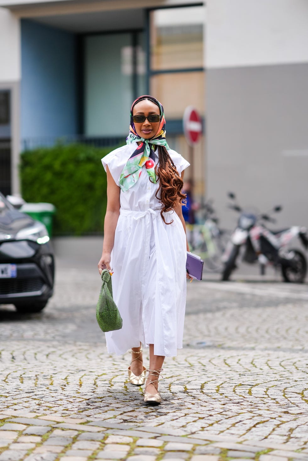paris, france june 20: a guest wears colorful pastel green bright red yellow floral pattern/print scarf, black sunglasses, white button up short sleeve midi dress, green knotted/pattern bag, silver rings, gold metallic flat lace up leather shoes, outside issey miyake, during the paris fashion week menswear spring/summer 2025 on june 20, 2024 in paris, france. (photo by edward berthelot/getty images)