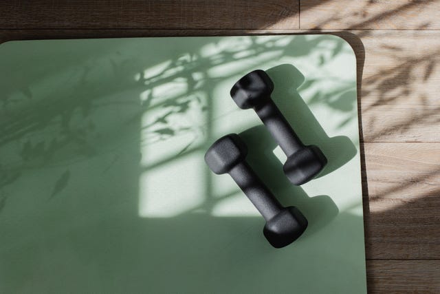 yoga mat and dumbbells on floor with shadow sunlight. fitness, wellness and home work out concept. high angle view with copy space